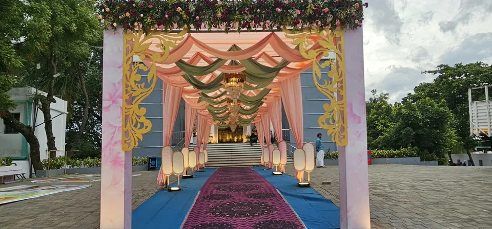 Outdoor pink canopy walkway with drapes, lanterns and blue carpet